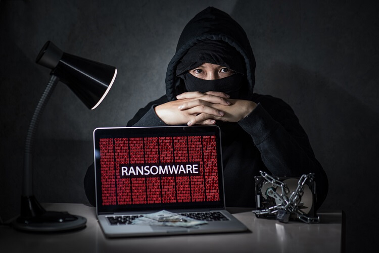 Hacker e notebook com ransomware na tela