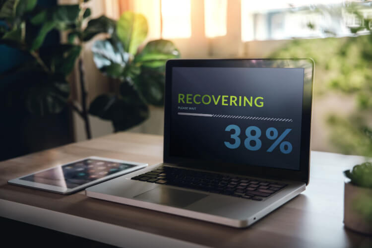 Laptop em cima de uma mesa, em processo de Disaster Recovery, escrito na tela "Recovering 38%".
